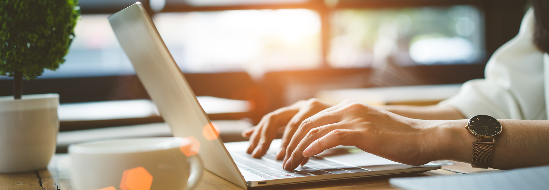 A woman writing a blog post from her laptop with a hot cup of coffee nearby.