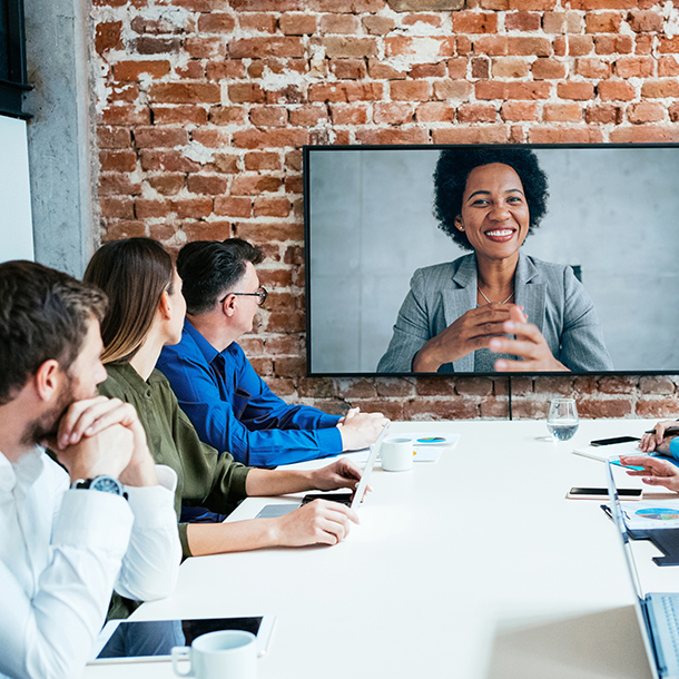 An in-person business meeting with a virtual guest included on the large television.