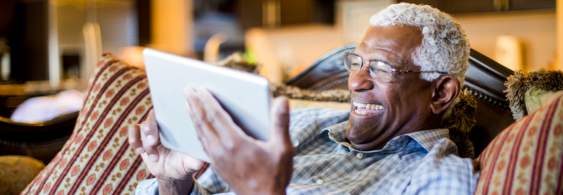 An older man enjoys watching a video on his tablet, while sitting comfortably on the couch.